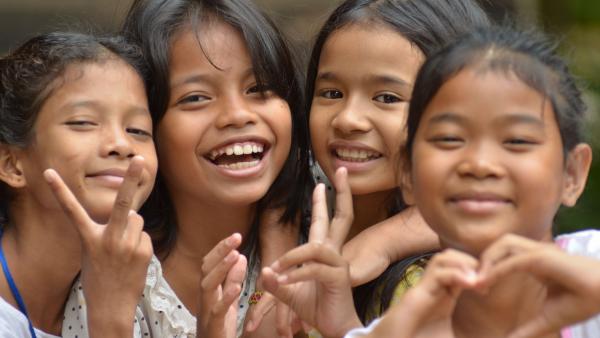 Quatre petites filles sourient et font des coeurs avec leurs mains
