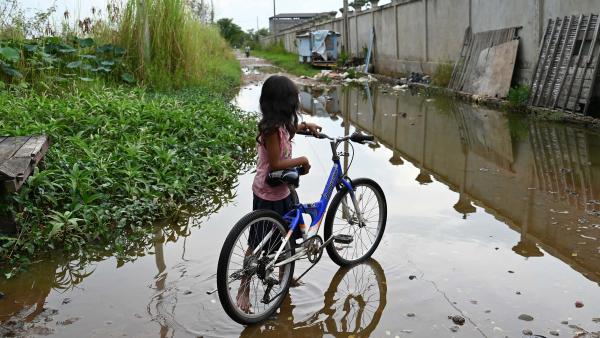 Une petite fille à côté de son vélo devant une ruelle inondée