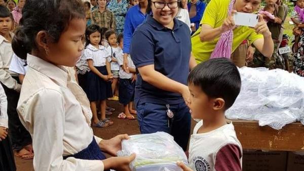 Leakhéna distributing school materials to two children cared for by PSE