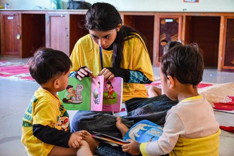 Les bébés regardent un livre d'images avec une monitrice des camps